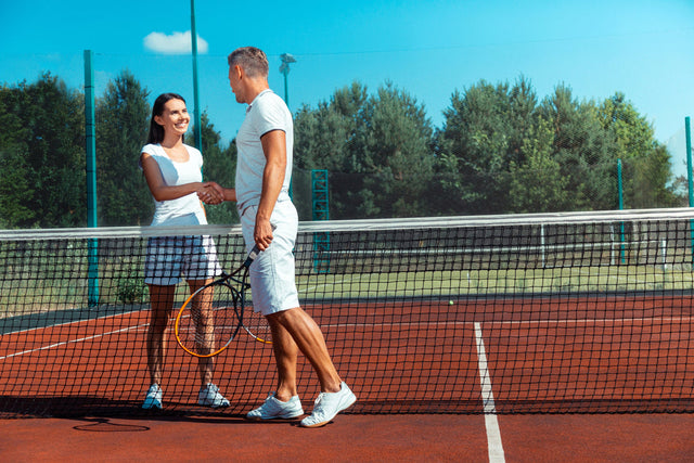 How long should tennis shorts be? A couple stands on a tennis court shaking hands after a match. 