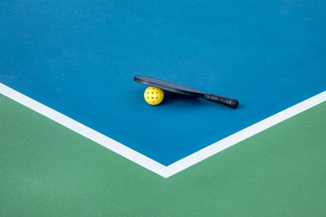 Learn more about the average time for a pickleball game. A pickleball paddle and ball sit on the corner of a court. 