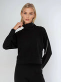 Woman wearing relaxed-fit funnel neck pullover with decorative silver zipper detail on left shoulder, showcasing the soft fabric drape and sporty-chic silhouette suitable for athletic and casual wear.  Front view.