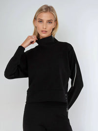 Woman wearing relaxed-fit funnel neck pullover with decorative silver zipper detail on left shoulder, showcasing the soft fabric drape and sporty-chic silhouette suitable for athletic and casual wear.  Front view.