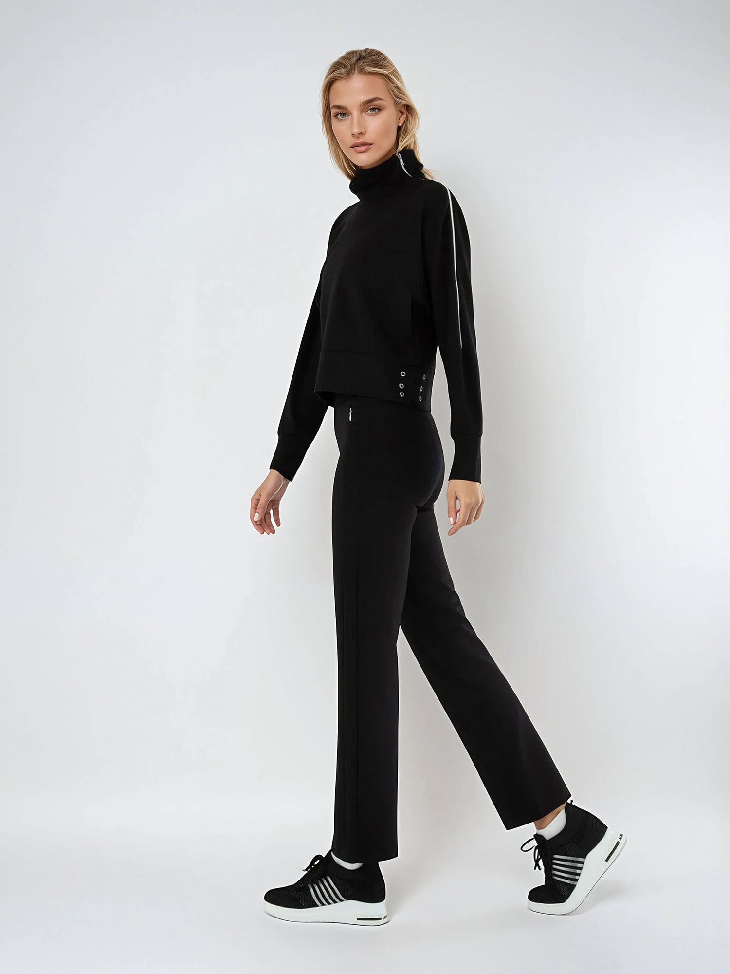 Woman wearing relaxed-fit funnel neck pullover with decorative silver zipper detail on left shoulder, showcasing the soft fabric drape and sporty-chic silhouette suitable for athletic and casual wear.  Left side full view.