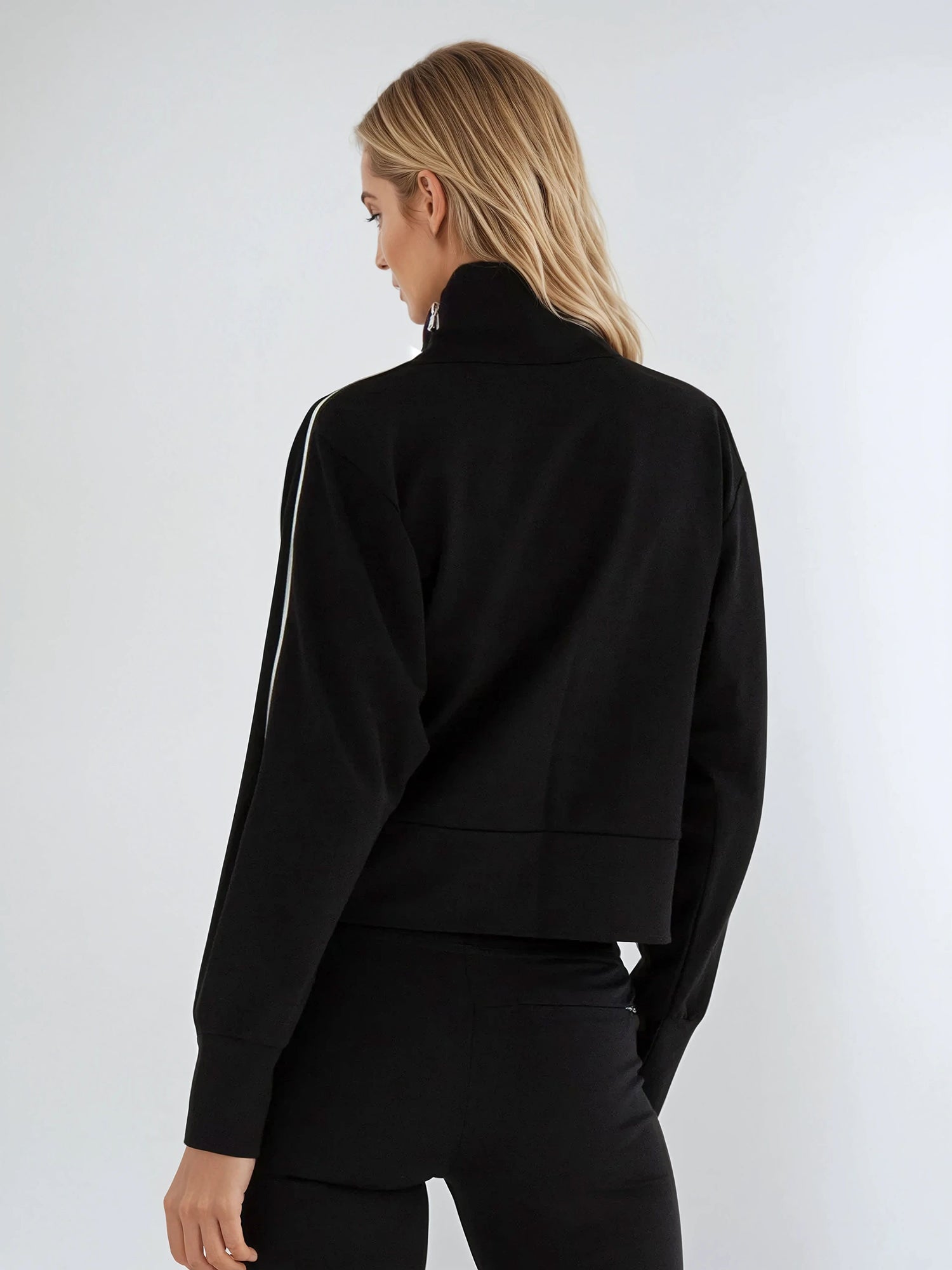 Woman wearing relaxed-fit funnel neck pullover with decorative silver zipper detail on left shoulder, showcasing the soft fabric drape and sporty-chic silhouette suitable for athletic and casual wear.  Back view.