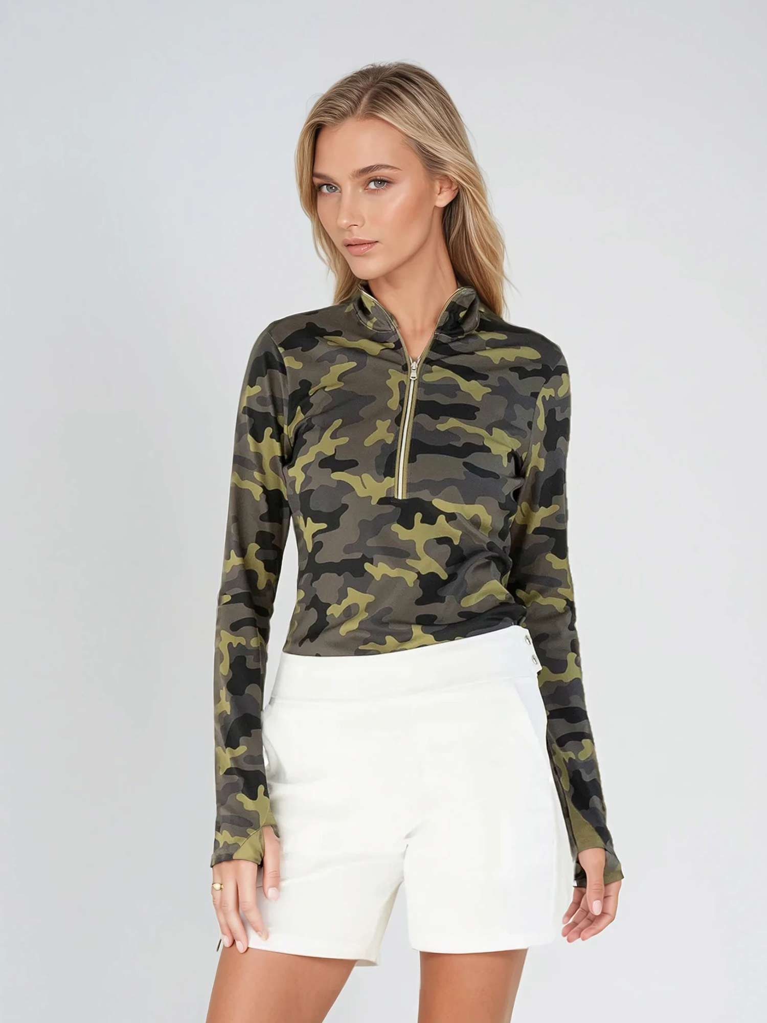 Woman wearing fitted camo print half-zip performance top with gold collar accents, thumbhole sleeves, and silver zipper detail, showcasing the versatile high collar design suitable for athletic and casual wear - front view shorts