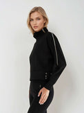Woman wearing relaxed-fit funnel neck pullover with decorative silver zipper detail on left shoulder, showcasing the soft fabric drape and sporty-chic silhouette suitable for athletic and casual wear.  Left side view.