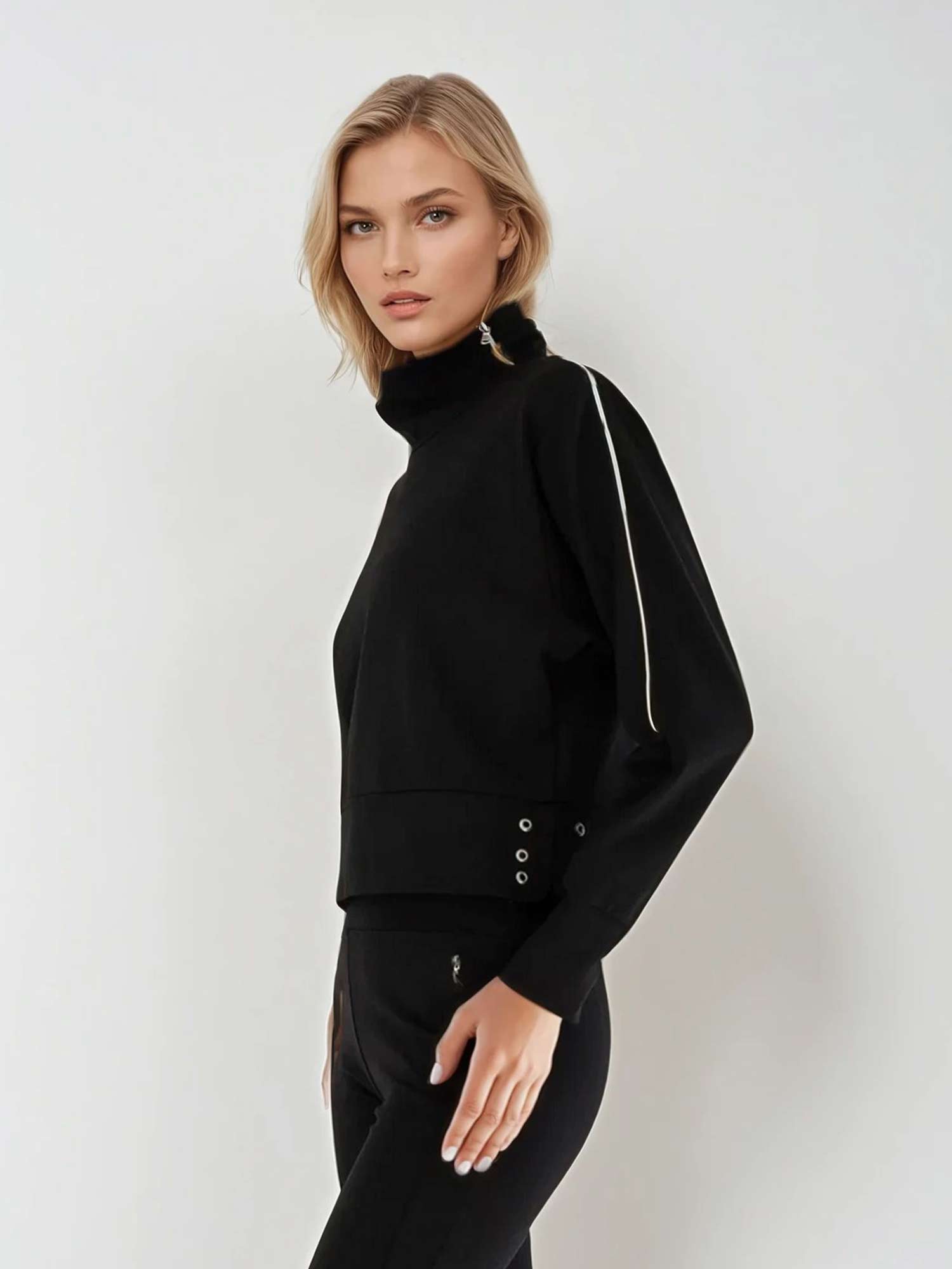 Woman wearing relaxed-fit funnel neck pullover with decorative silver zipper detail on left shoulder, showcasing the soft fabric drape and sporty-chic silhouette suitable for athletic and casual wear.  Left side view.