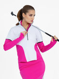 Front view of model wearing the Logan performance long in white and pink by inPhorm NYC with one hand on her zipper and the other holding a golf club