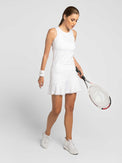 Front view of model wearing the tennis classic 15" flounce skirt in white by inPhorm NYC wearing white shoes, white wrist band, and holding a tennis racket