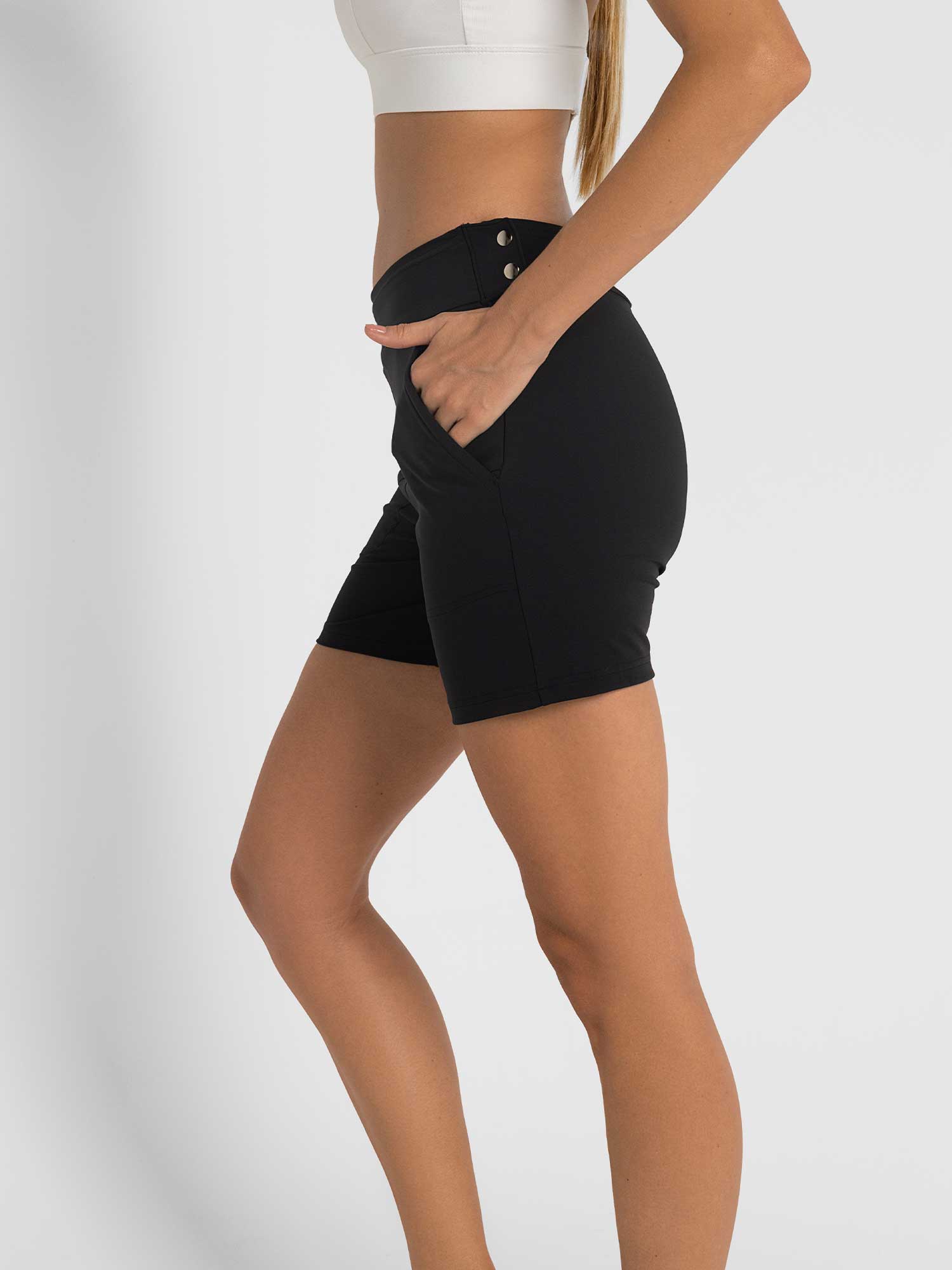 Side view of model wearing the womens golf shorts in black by inPhorm NYC with her hands in her pockets