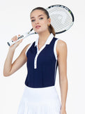 Front view of model wearing the Alexa performance sleeveless polo in ink and white by inPhorm NYC with a tennis racket in her hand over her shoulder