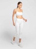 Front profile view of model wearing the Zone capri leggings in white and silver by inPhorm NYC wearing matching bra and shoes