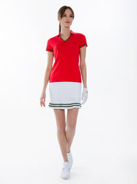 Front view of model wearing the Fairway v-neck collar top in poppy and militaire  by inPhorm NYC with her hands at her side wearing a white skirt