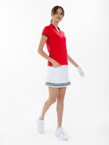 Front view of model wearing the Fairway v-neck collar top in poppy and militaire by inPhorm NYC with her hands at her side wearing a white skirt