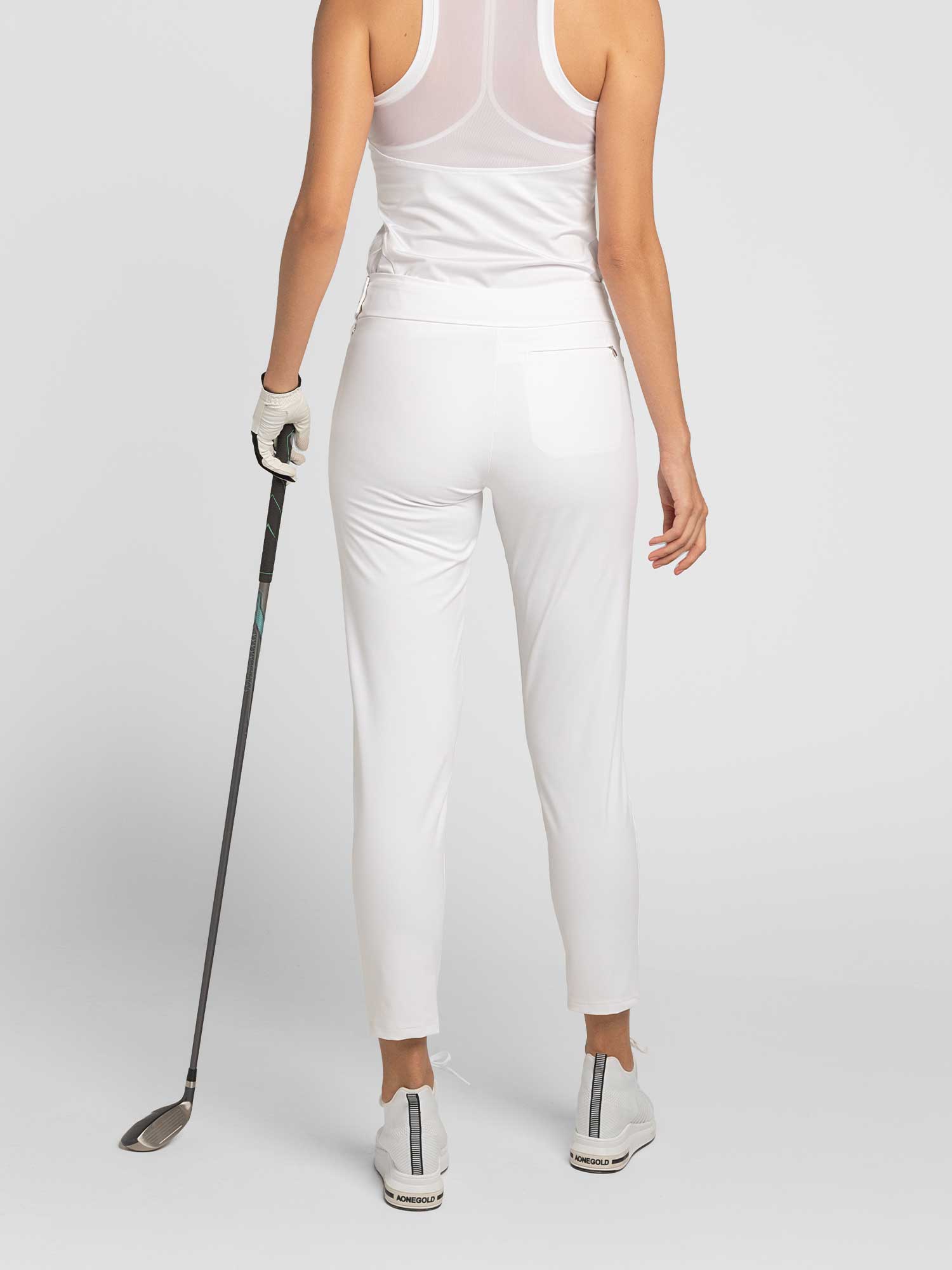 Back view of model wearing the swing Cleo pants in white by inPhorm NYC holding a golf club wearing a white top