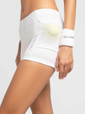 Front view of model wearing the tennis ace shorts in white by inPhorm NYC with a tennis ball in her pocket wearing a white wrist band