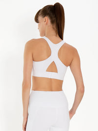 Back view of model wearing the Ashley high impact bra in white by inPhorm NYC with her hands in her pockets