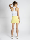 Back view of model wearing the Aubrey 13 1/2 tennis skirt in lemonade by inPhorm NYC with one hand on her head