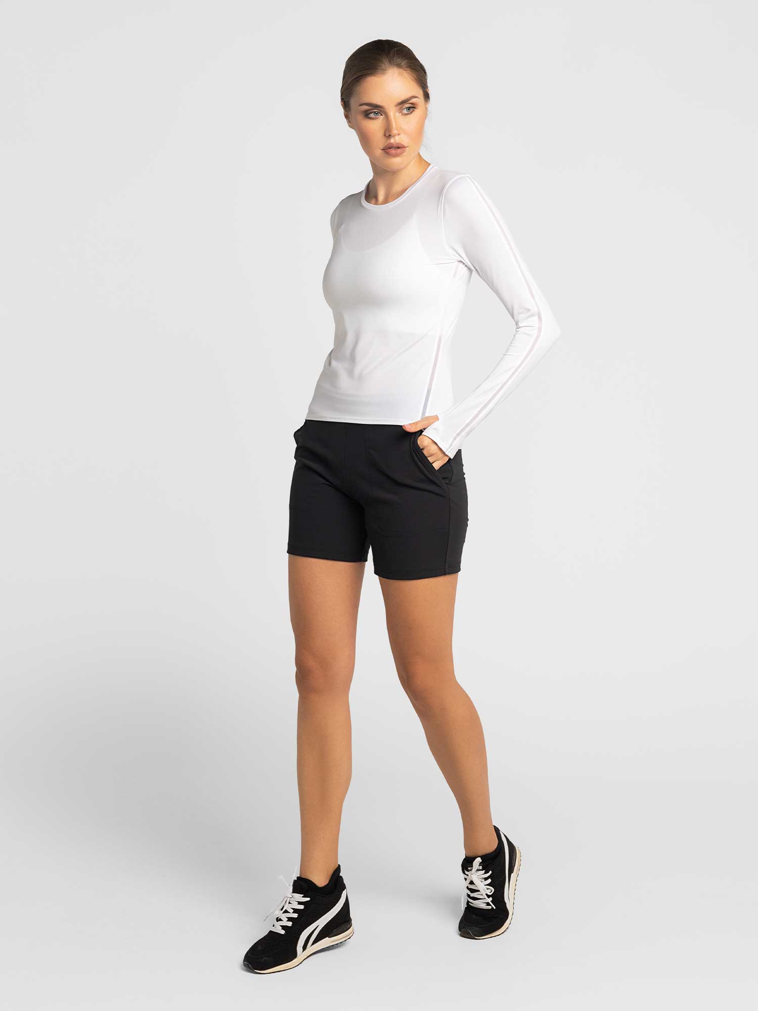 Front view of model wearing the classic long sleeve crew in white by inPhorm NYC wearing black shorts with one hand in her pocket