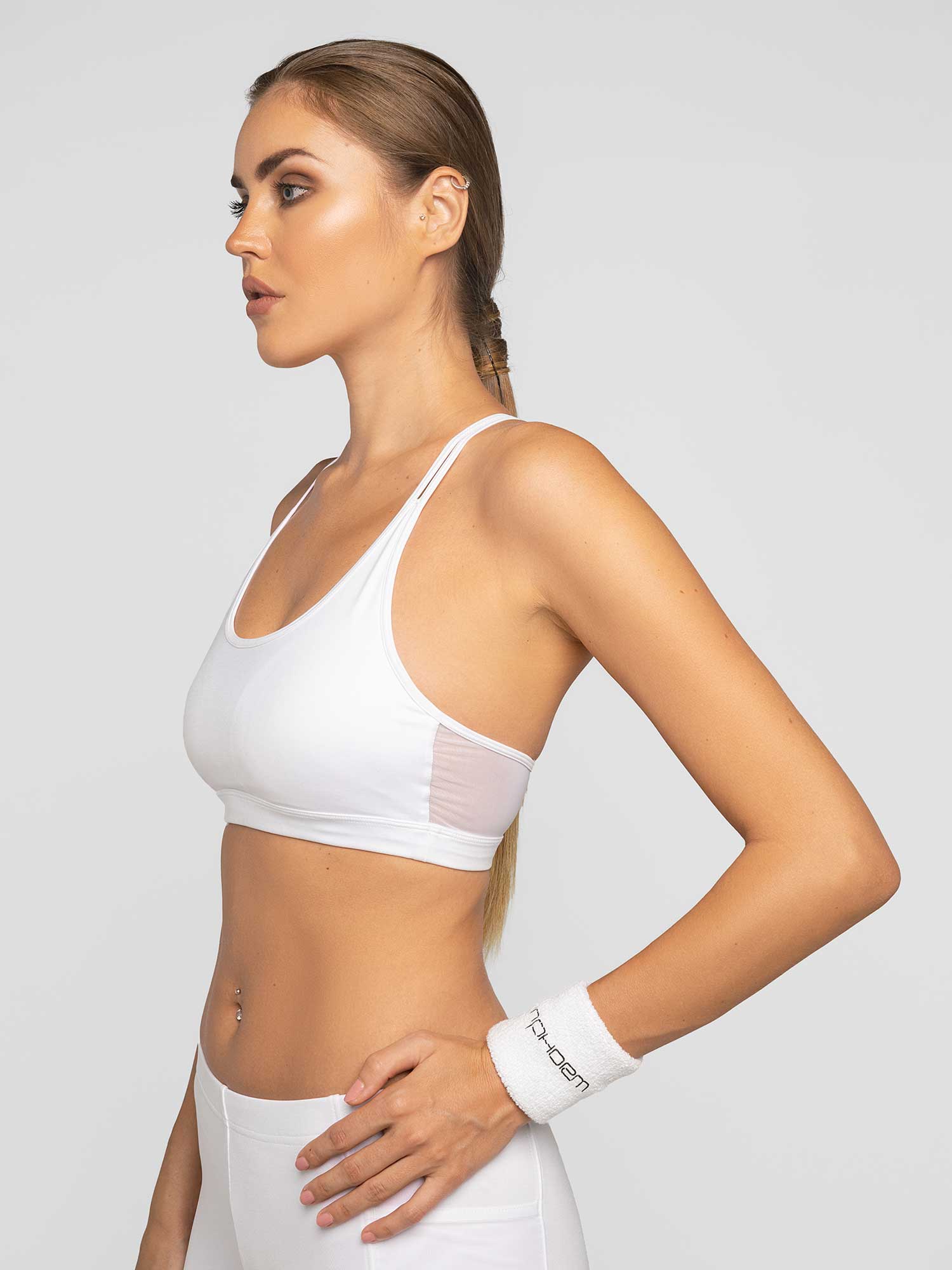 Side view of model wearing the classic strappy bra in white by inPhorm NYC with one hand on her hip