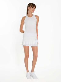 Front view of model wearing the courtside charm tennis skirt in white by inPhorm NYC with one hand behind her back and one at her side