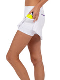 Side view of model wearing the Sinclaire 13 1/2" pleated hem golf and tennis skirt in white/imperial by inPhorm NYC holding a yellow tennis ball in her pocket