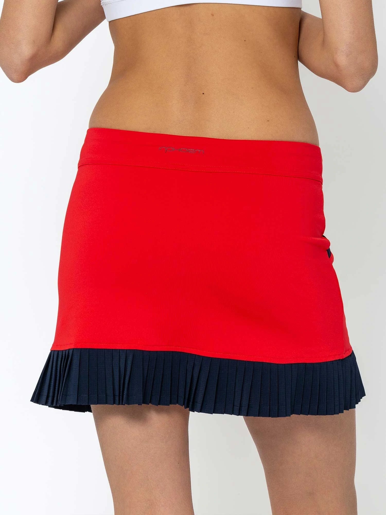 Front view of model wearing the Kai 15" pleated skirt in poppy and midnight by inPhorm NYC with her arms bent