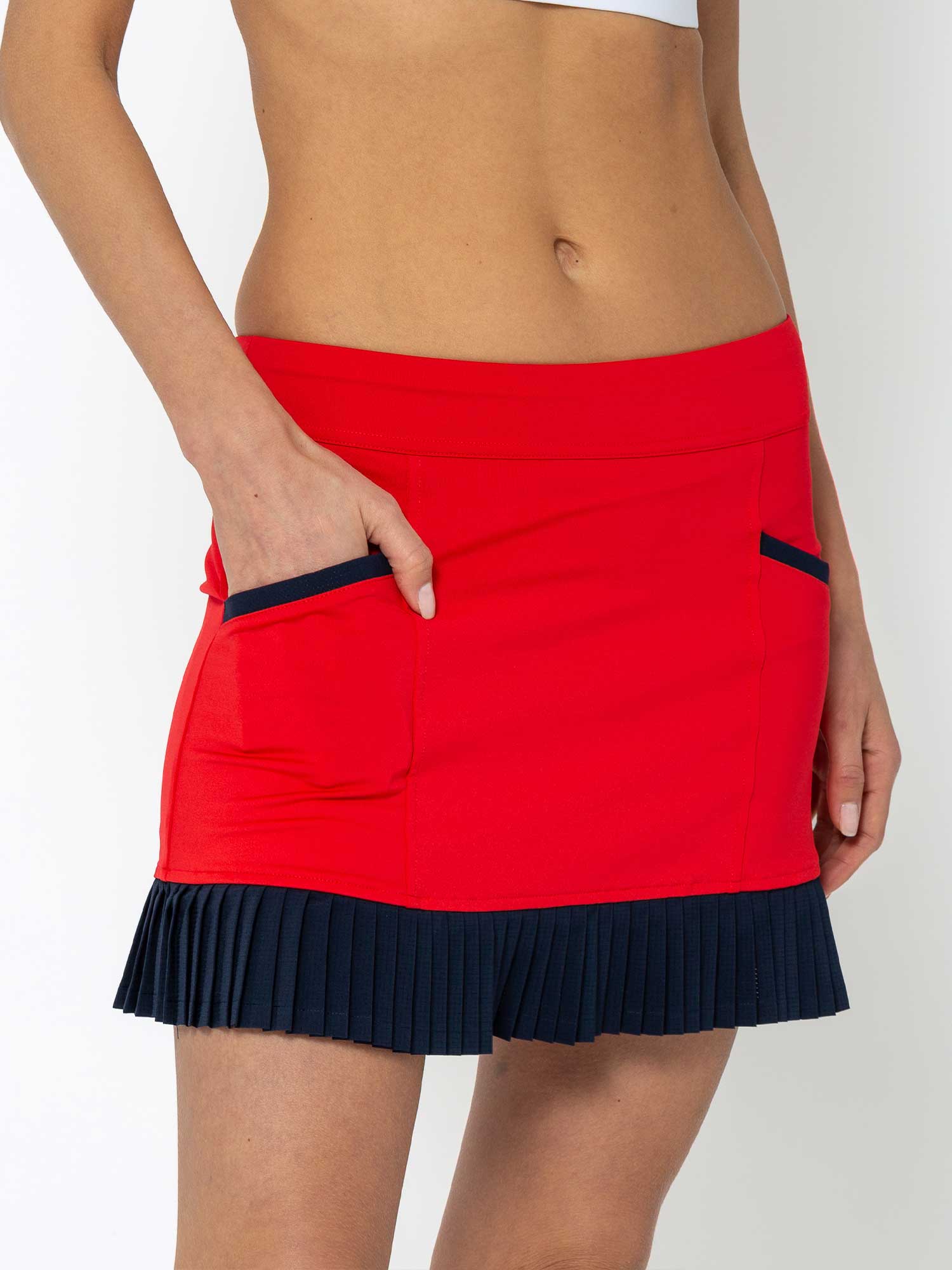 Front view of model wearing the Kai 17" pleated skirt in poppy and midnight by inPhorm NYC with one hand in her pocket