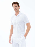 Front view of model wearing the performance mens classic tennis rib collar polo in white poppy and militare by inPhorm NYC with one hand in his pocket