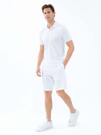 Front view of model wearing the performance mens classic tennis rib collar polo in white poppy and militare by inPhorm NYC wearing white shoes with one hand in his pocket