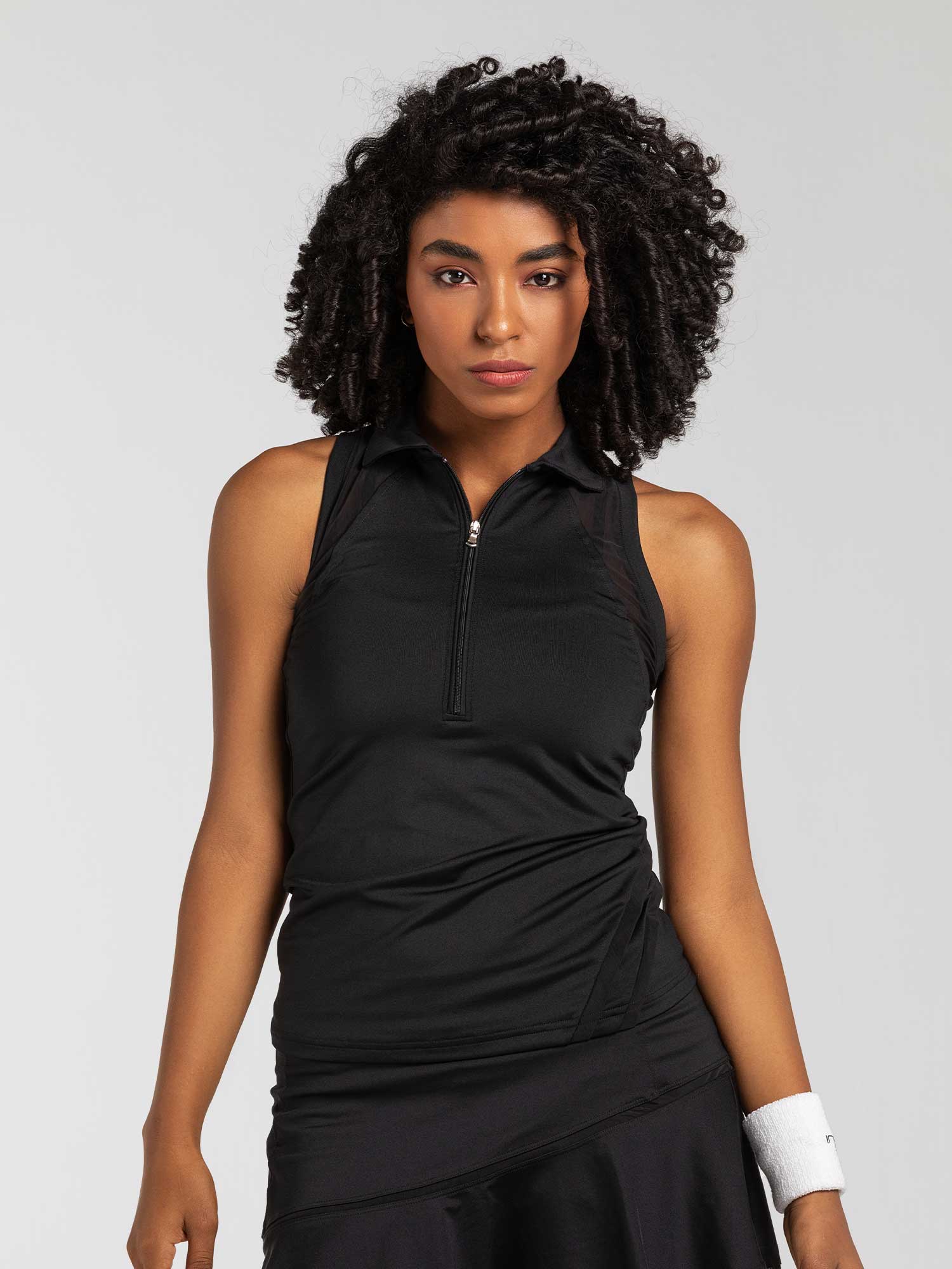 Front view of model wearing the Neisha classic sleeveless polo in black by inPhorm NYC with her hands at her side