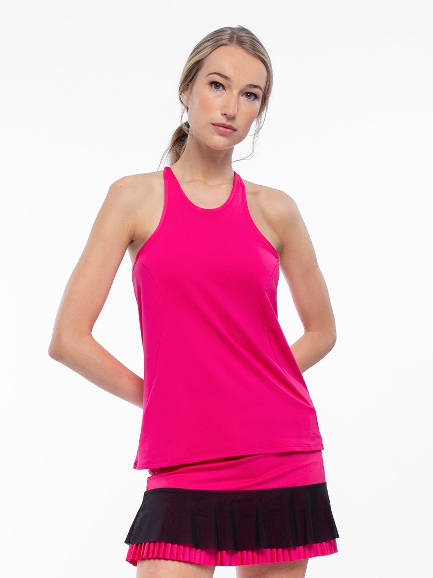 Front view of model wearing the Nora halter neck active and tennis tank in fuchsia by inPhorm NYC with her hands behind her back