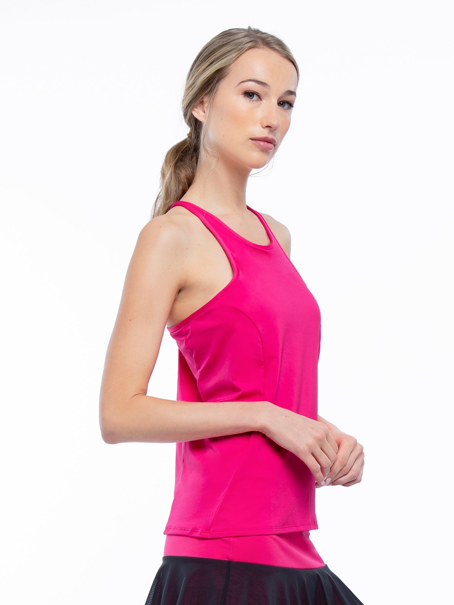 Side view of model wearing the Nora halter neck active and tennis tank in fuchsia by inPhorm NYC with her hands together