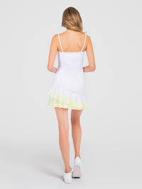 Back view of model wearing the pearl adjustable strap tennis dress in white zest ombre a by inPhorm NYC with her amrs bent