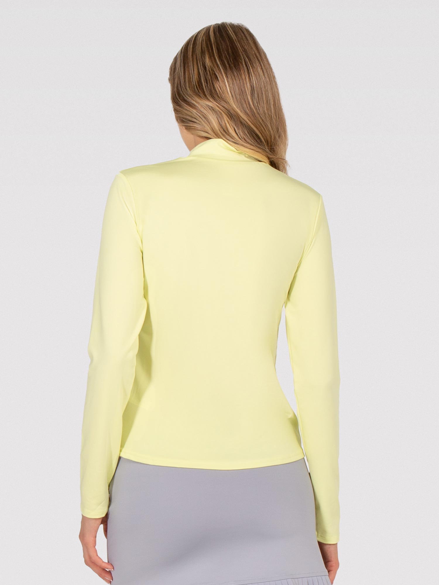 Back view of model wearing the Riley performance mock neck in zest combo by inPhorm NYC with her hands at her side