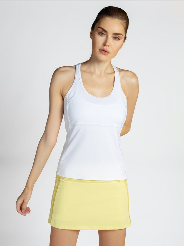 Front view of model wearing the Ashley racer tank in white by inPhorm NYC wearing zest color skirt